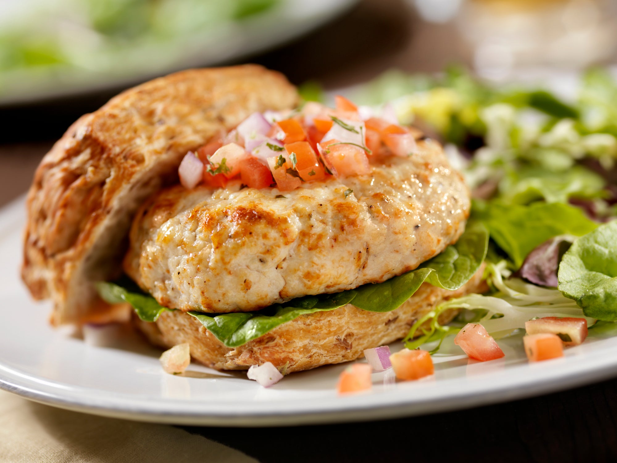 A plated dish featuring a boneless, skinless chicken breast topped with tomato and onion, served alongside a salad.